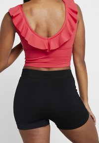 Top corto rosso con dettagli a volant e scollatura profonda sul retro, abbinato a pantaloni corti neri a coste. Concentrati sui colori vivaci e sui tessuti in contrasto.