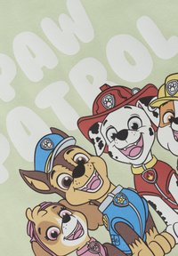 Illustrationen visar fyra tecknade hundar i olika färgade uniformer på en ljusgrön bakgrund, tillsammans med texten "PAW PATROL" i vitt.