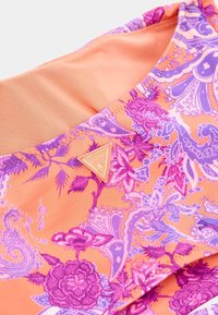 Večbarvna tkanina z oranžno podlago in vijoličnimi cvetličnimi ter paisley vzorci. Vključuje triangularni zlat akcent z napisom "GUESS".