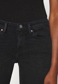 Jeans de mezclilla negra con un diseño clásico, que presentan un cierre frontal con botón y cremallera, cinco bolsillos y detalles de costura sutiles.