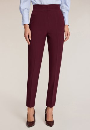 Femme portant un pantalon slim taille haute bordeaux, associé à des escarpins assortis et une chemise bleue rayée.