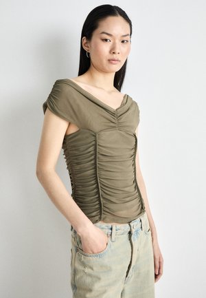 Olive green, fitted top with a V-neck, short sleeves, and ruching along the front and sides; paired with light blue jeans.