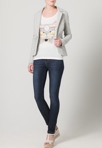 Jasnoszara marynarka na białej koszulce z kolorowym nadrukiem lisa, zestawiona z ciemnoniebieskimi obcisłymi dżinsami i koturnami espadrylowymi.