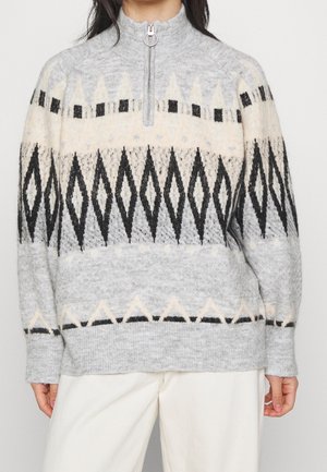Pull en laine avec col à demi-fermeture éclair, présentant des motifs géométriques en forme de losange noirs et crème sur fond gris clair.