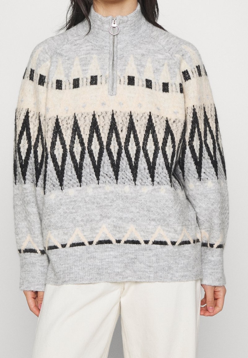 Pull en laine avec col à demi-fermeture éclair, présentant des motifs géométriques en forme de losange noirs et crème sur fond gris clair.