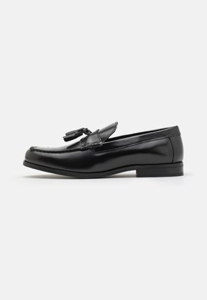 Black leather loafers with a smooth finish, tasseled accents, and a stitched design on the toe. Slight heel and rounded shape.