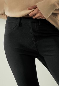 Černé džíny z denimu s rozšířeným designem, obsahující přední kapsy, poutka na opasek a hladkou texturu, v kombinaci s béžovým svetr.
