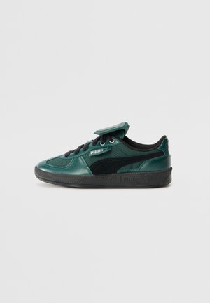 Baskets basses Puma vert foncé et noir avec lacets noirs et semelle texturée, vues de côté sur un fond clair uni.