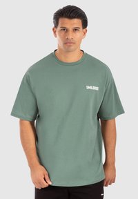 Grøn bomulds t-shirt med en afslappet pasform, rund halsudskæring og korte ærmer. Har et hvidt "SMILODOX" logo på venstre brystområde.