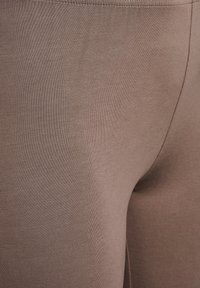 Leggings marroni elasticizzati con una texture liscia e un design aderente. Cuciture visibili lungo la vita e le cuciture laterali.