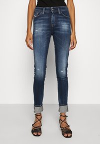 Jeans de corte ajustado, azules oscuros, hechos de mezclilla con un acabado desvaído y desgastado, y puños enrollados. Presentan bolsillos estándar y cierre de botón.