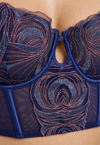 Reggiseno blu navy con rete trasparente e intricato ricamo floreale in blu e oro rosa. Dettaglio a chiave sul davanti, accenti in raso.