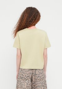 Κοντομάνικο, ανοιχτό κίτρινο T-shirt με στρογγυλή λαιμόκοψη. Εμφανίζεται από πίσω, συνδυασμένο με σορτς με λεοπάρ σχέδιο. Ομαλή υφή, άνετη εφαρμογή.