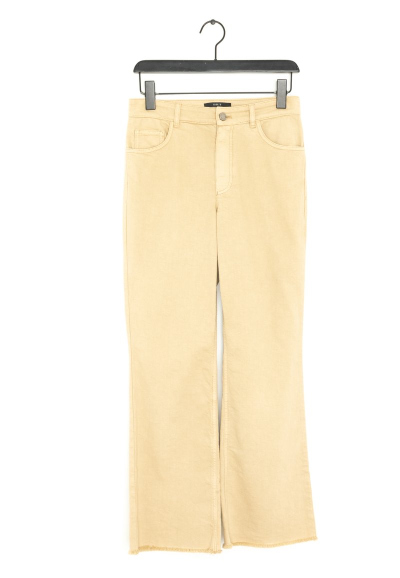Jeans beige a zampa d'elefante in cotone. Presentano tasche frontali, chiusura con zip e orlo sfilacciato. Texture liscia con una finitura leggermente sfumata.