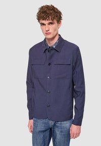 Giacca blu navy con maniche lunghe, chiusura frontale con bottoni e due tasche sul petto. Realizzata in materiale liscio con vestibilità comoda.