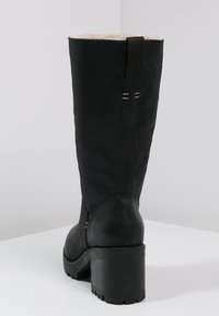 Bota negra hasta la rodilla con un material texturizado, forro de piel sintética y un tacón cuadrado. Presenta dos acentos de costura decorativa en la parte posterior.