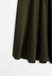 Jupe en tissu vert foncé avec une texture lisse et un ourlet évasé, présentée sur fond blanc.