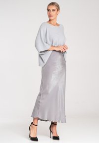 Hellgrauer oversize Pullover mit Fledermausärmeln, kombiniert mit einem glänzenden silbernen Satinkleid. Schwarze High Heels runden das Outfit ab.