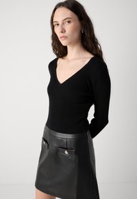 Pull en maille noir avec un décolleté en V profond, associé à une mini-jupe en cuir noir dotée de deux poches avant et d'accents métalliques.