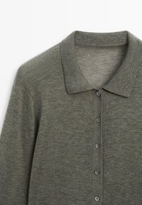 Dunkelgrünes Strickpolo mit weicher Textur, Kragen und sechs Knöpfen. Besitzt ein dezentes meliertes Muster.