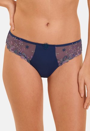 Woman wearing navy blue hipster panties with sheer floral lace panels and a small decorative flower at the center front waistband.