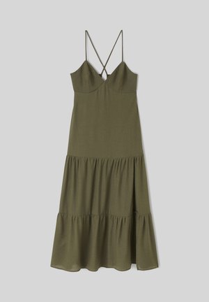 Robe midi sans manches vert olive avec fines bretelles croisées, corsage ajusté et jupe à volants superposés sur fond gris clair.