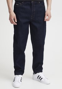 Temno modre denim hlače z ohlapno prileganjem, z oranžnim šivom in žepi. Združene z belimi supergami s črnimi črtami.