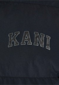 Material negru cu "KANI" imprimat cu un font îndrăzneț, gri. Textura este netedă, cu un ușor luciu, având cusături curate pe margini.