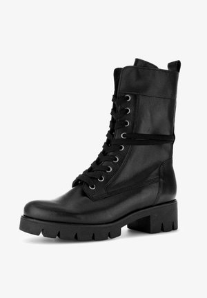 Bottine en cuir noir à lacets avec un talon épais, un col rembourré et une semelle en caoutchouc texturée. Œillets argentés soutenant des lacets ronds.