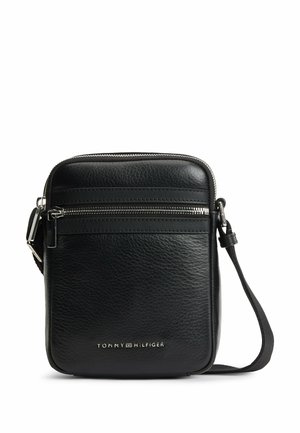 Black textured leather crossbody bag with front zipper pocket, adjustable strap, and silver Tommy Hilfiger logo at the bottom center.