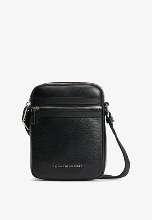Sac bandoulière en cuir noir texturé avec poche avant zippée, sangle réglable et logo Tommy Hilfiger argenté en bas au centre.
