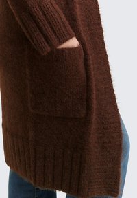 Brązowy dziany kardigan z prążkowanymi mankietami i krawędzią, wyposażony w dużą przednią kieszeń oraz miękkie, teksturowane wykończenie.