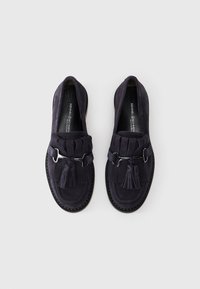 Mocassins en suede bleu marine foncé avec un design en franges texturé, des pompons décoratifs et des accents en métal argenté. Semelle en caoutchouc pour une meilleure adhérence.