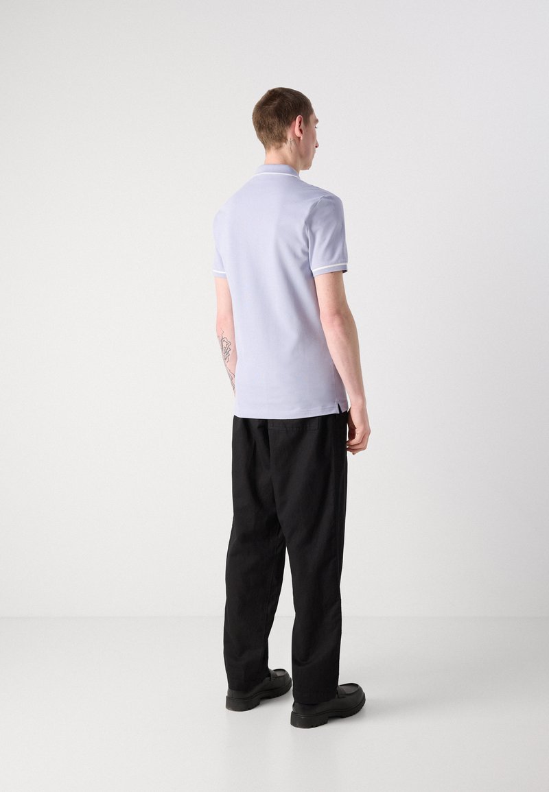 Hellblaues Poloshirt mit kontrastierendem weißen Besatz, kurzen Ärmeln und schmaler Passform. Tragen Sie dazu schwarze weit geschnittene Hosen und schwarze Schuhe.