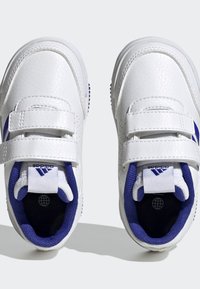 Zapatillas sintéticas blancas con acentos morados, doble tira de Velcro, acabado texturizado y suela de goma con pequeños puntos de tracción.