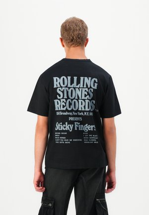 Black cotton T-shirt featuring large white text on the back, displaying "Rolling Stones Records" and song titles from "Sticky Fingers."