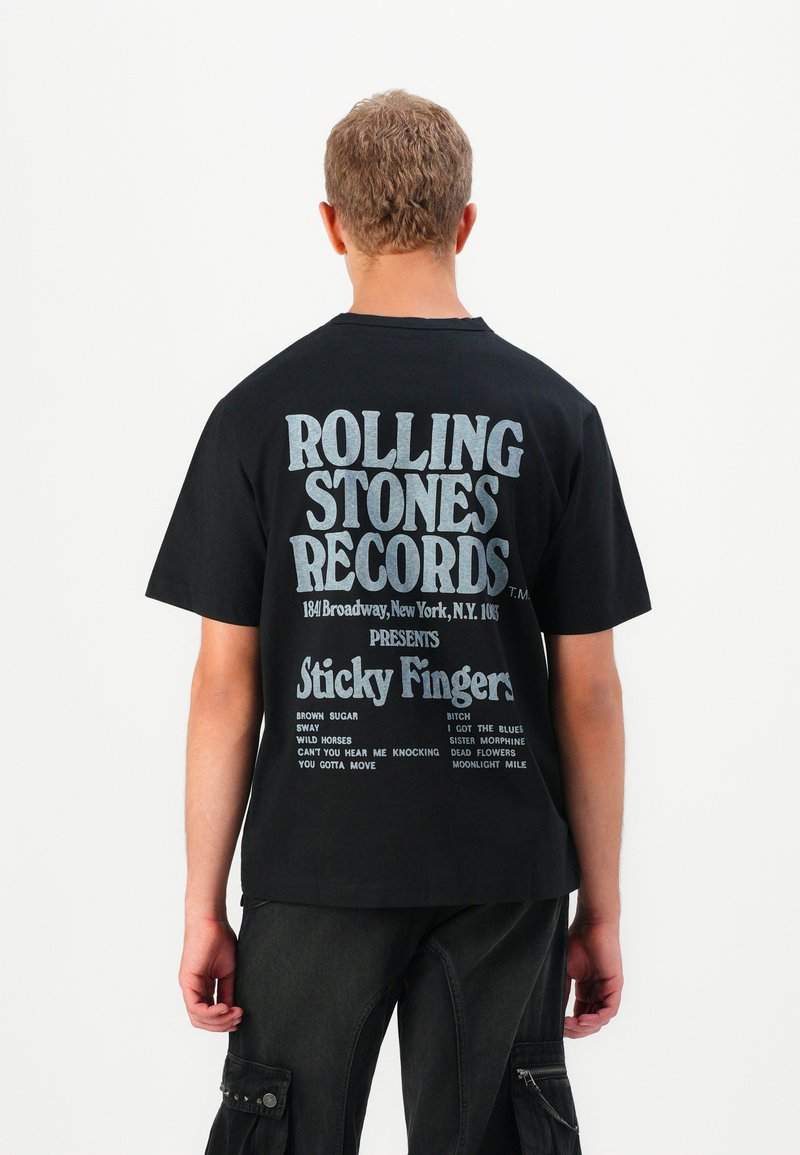 Czarna bawełniana koszulka z dużym białym napisem na plecach, wyświetlająca "Rolling Stones Records" oraz tytuły utworów z albumu "Sticky Fingers."