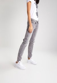 Grå raka jeans med framlommor, bälteshällor och en mjuk textur. Kombinerat med en vit t-shirt med grafiskt tryck och vita sneakers.