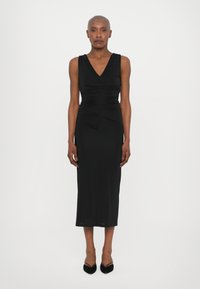 Robe noire ajustée sans manches avec un décolleté en V profond, des détails froncés à la taille et une longueur au genou. Matière douce et lisse ; design minimal.