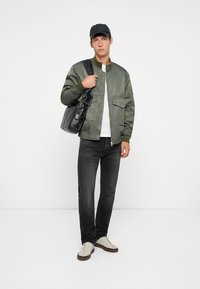 Green bomber jacket, white shirt, black jeans, beige sneakers, and black bag. The jacket features a smooth texture and ribbed cuffs.