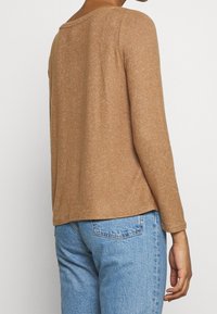 Maglione marrone a maniche lunghe con una vestibilità rilassata, realizzato in un tessuto a maglia testurizzato, con scollatura rotonda e orlo leggermente accorciato.