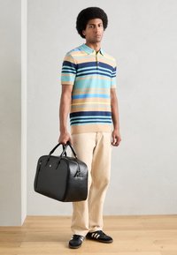 Polo majica sa prugama u plavoj, žutoj i krem boji; svijetlosmeđe hlače; elegantna crna torba za sportske aktivnosti; crni tenisice s bijelim prugama.