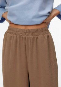 Pull bleu clair associé à un pantalon marron ample avec une ceinture élastique et un tissu doux et texturé.
