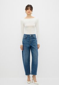 Jeans de mezclilla azul de talle alto con un corte relajado, combinados con una blusa ajustada de manga larga blanca y tacones de color claro.