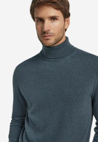 Ciemnoniebieski sweter z golfem wykonany z drobnej dzianiny, z wysokim kołnierzem i długimi rękawami o gładkiej fakturze.