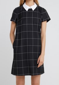 Svart klänning med korta ärmar, vit krage och rutmönster i vita linjer. Mjuk tyg med sidfickor. Enkel A-linjeform.