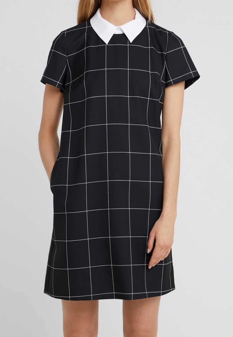 Schwarzes Kleid mit kurzen Ärmeln, weißem Kragen und Karomuster in weißen Linien. Weicher Stoff mit seitlichen Taschen. Einfacher A-Linien-Schnitt.