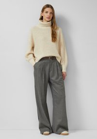 Kremowy, dziergany golf o luźnym kroju, zestawiony z szarymi szerokimi spodniami w prążki i jasnymi butami. Akcent w postaci brązowego paska.
