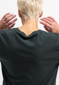 Donkergroen T-shirt met korte mouwen en een ronde halslijn; heeft een klein, lichtgrijs schaarlogo aan de achterkant nabij de kraag.