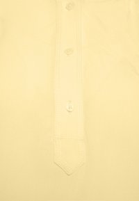 Camicia gialla chiara con parte anteriore dotata di una chiusura a bottoni verticale con tre bottoni e cuciture decorative attorno alla placca.